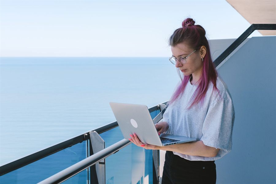 Woman using a laptop at the rail of a sea-view terrace