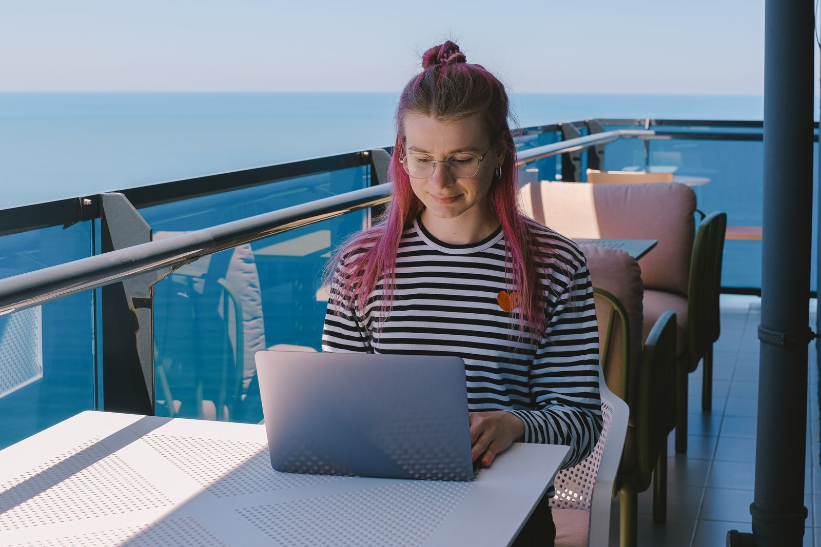Woman working on a laptop at a sunny oceanfront balcony table
